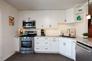 A modern kitchen with white cabinetry, stainless steel appliances, and a granite countertop. - The Sunny Casita + Zoo + Spa + Views + Downtown (San Diego)