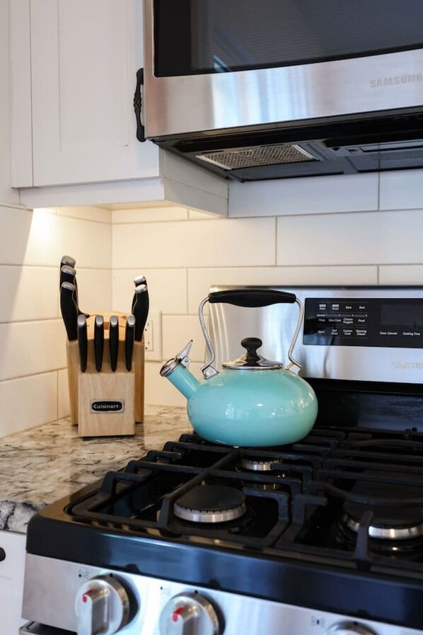 Una cocina con estufa a gas, microondas de acero inoxidable y tetera color turquesa.