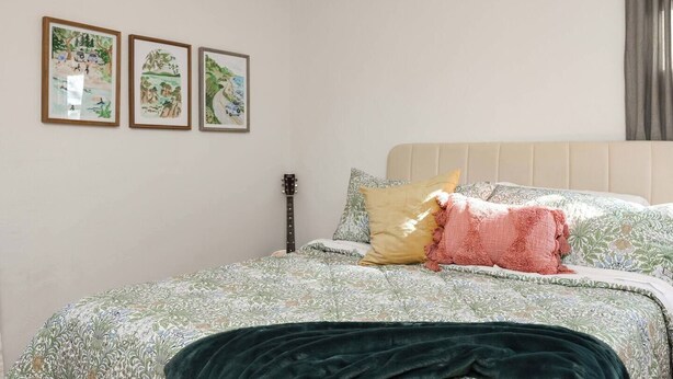 Una camera da letto con un letto, cuscini, una chitarra e tre quadri appesi al muro.