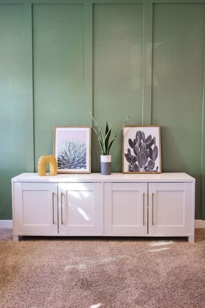 A white cabinet with three framed pictures and a potted plant against a green wall. - The Sunny Casita + Zoo + Spa + Views + Downtown (San Diego)