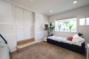 Un dormitorio con cama, una ventana con plantas, un radiador y una escalera.