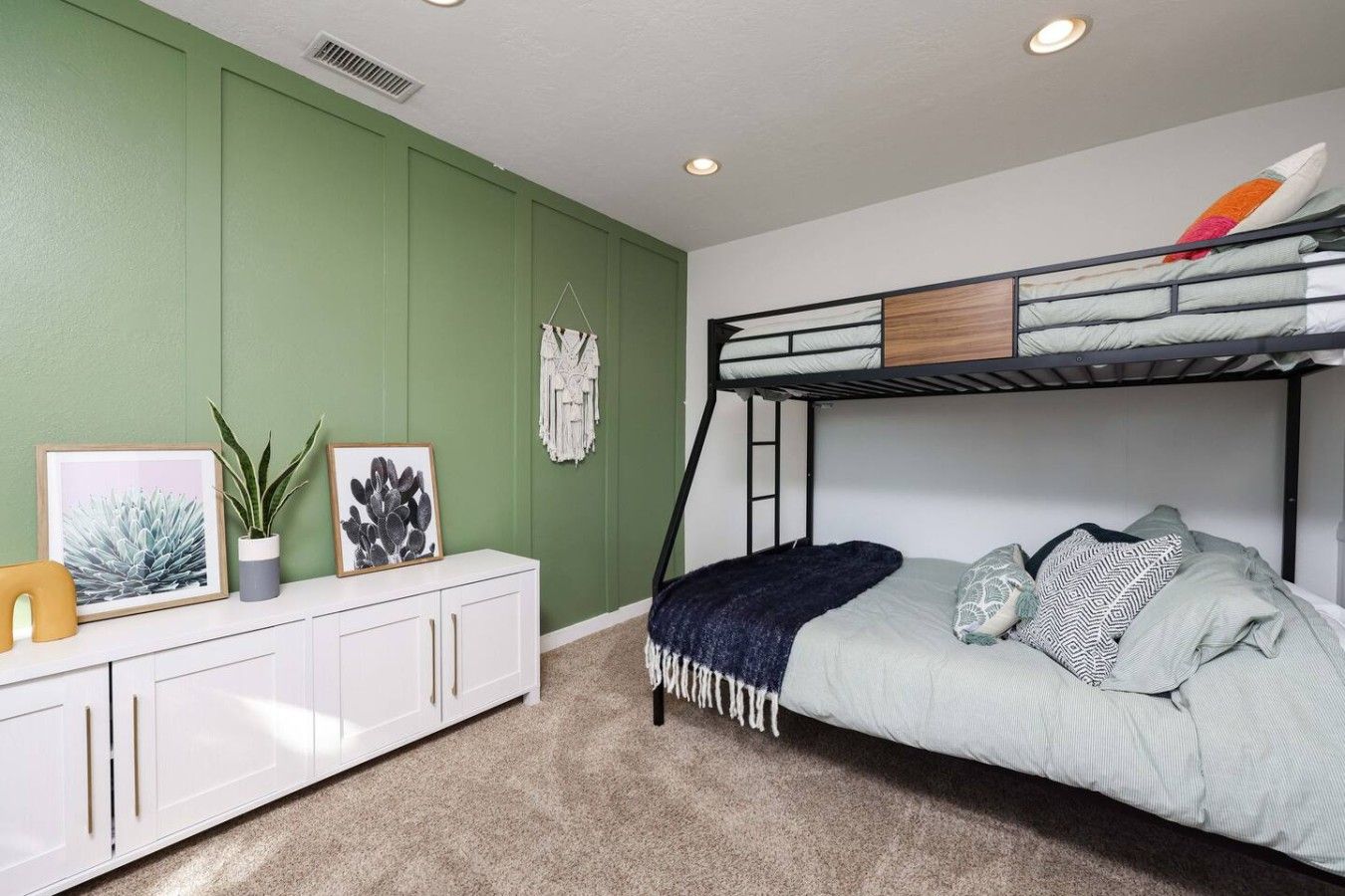 Una cama litera con escalera, un armario blanco con cajones, una planta en maceta y cuadros en la pared.