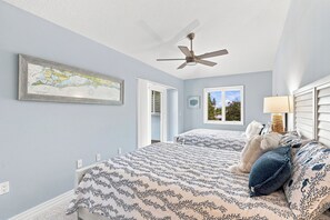 Ein Schlafzimmer mit Deckenventilator, einem Bett mit gemustertem Bettbezug, einem Fenster mit Blick und einer an der Wand hängenden Karte.