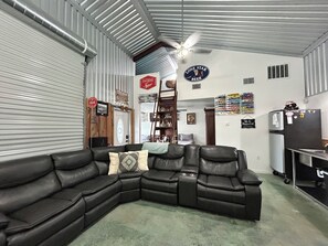 A room with a sectional sofa, a ceiling fan, a refrigerator, and various wall decorations.