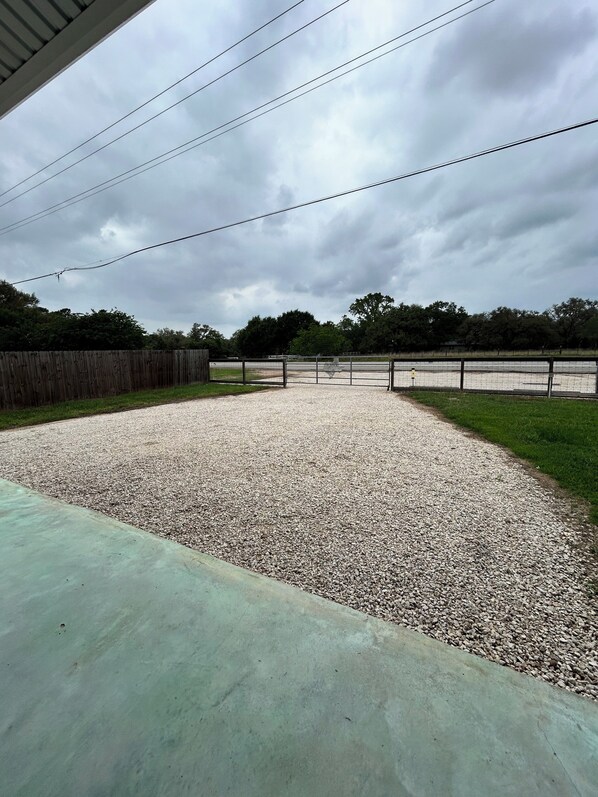 A gravel arena with a fence, surrounded by trees and a wooden fence.