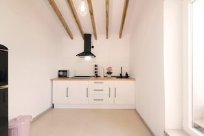 A compact kitchen with white cabinetry, a black range hood, a countertop with a toaster, and a pink trash bin. - El Patio de Rafaela Country House with Mountain Views, Wi-Fi and Air Conditioning (Alcaucín)