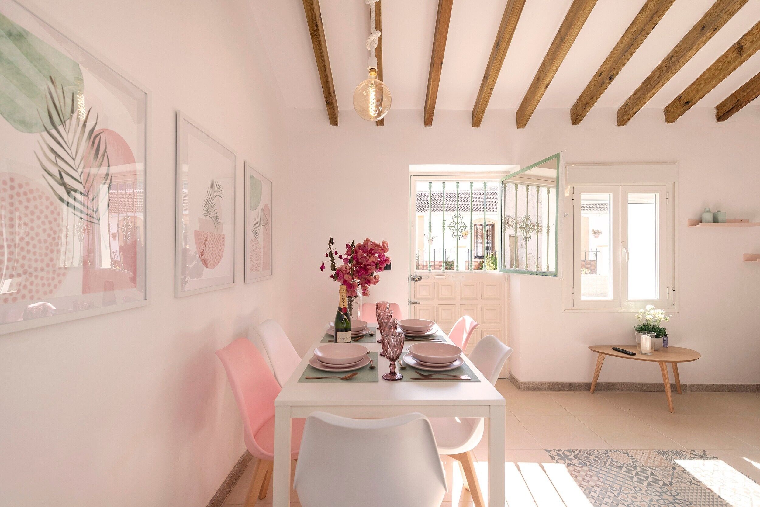 Un coin repas avec une table dressée pour quatre personnes, des chaises, une fenêtre donnant sur un beau paysage et une petite table sur laquelle se trouve une télécommande.