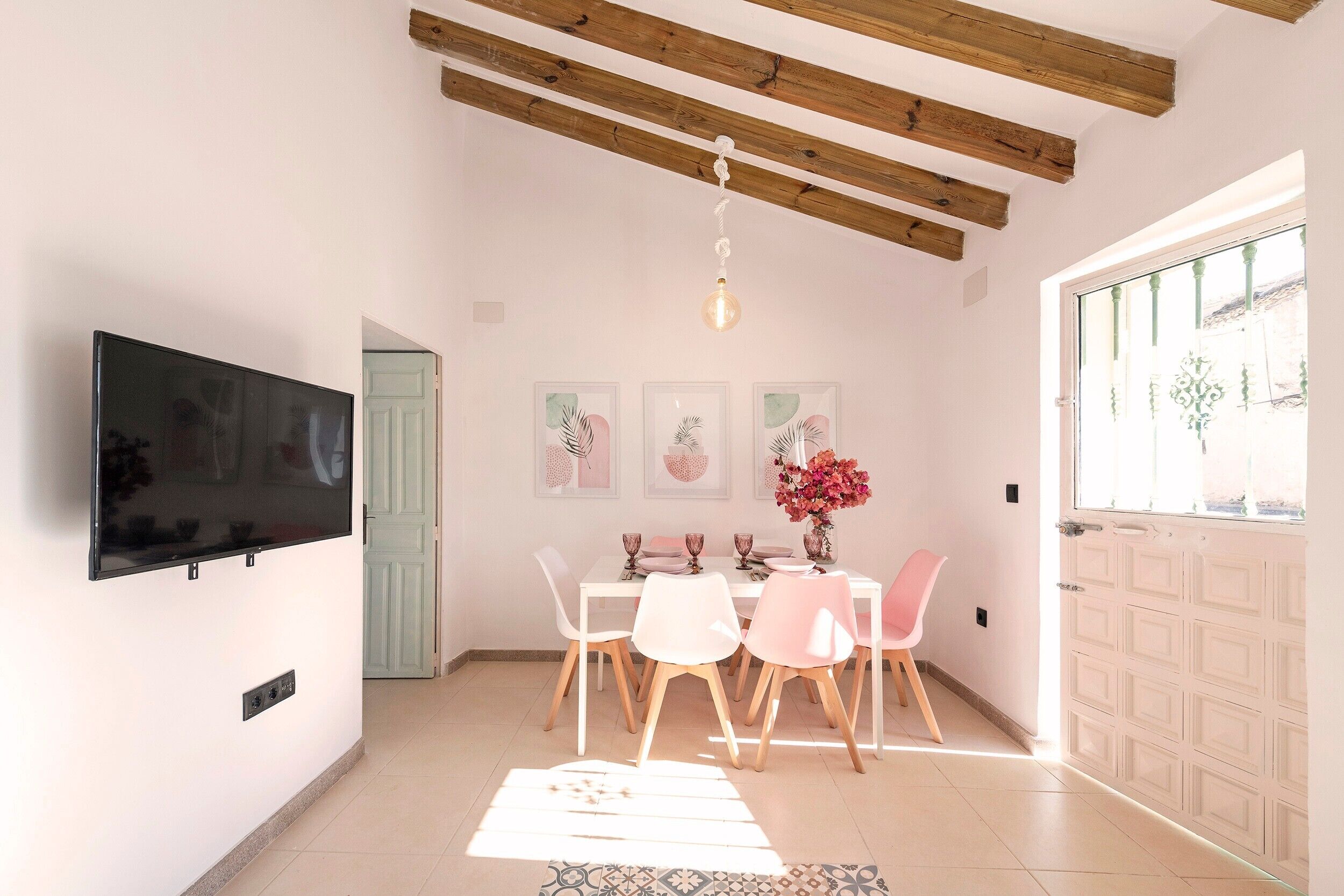Un coin repas avec un téléviseur fixé au mur, une table dressée pour quatre personnes et une porte donnant sur l’extérieur.