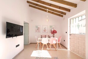 A dining area with a TV mounted on the wall, a table set for four, and a door leading outside. - El Patio de Rafaela Country House with Mountain Views, Wi-Fi and Air Conditioning (Alcaucín)