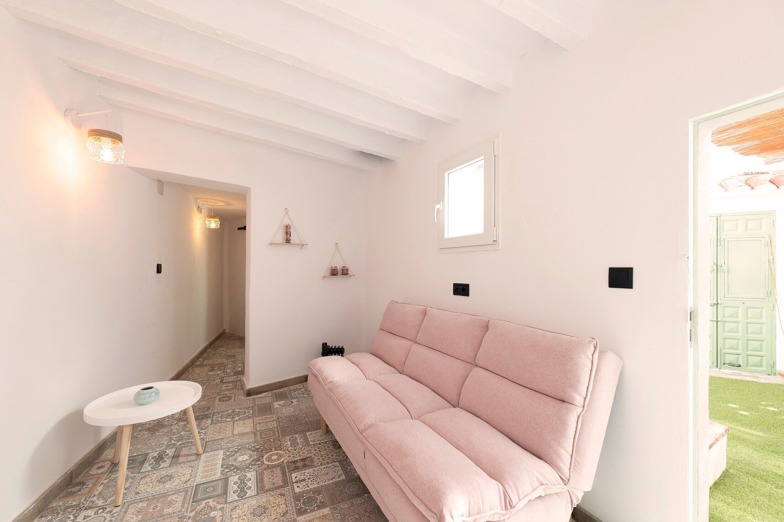 A room with a patterned floor, a pink sofa, a small round table, and a door leading outside.