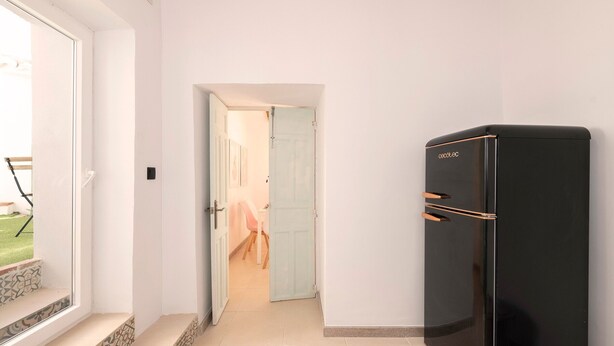 A hallway with a black refrigerator, a door leading to a room with a chair, and a window with a view of the outdoors. - El Patio de Rafaela Country House with Mountain Views, Wi-Fi and Air Conditioning (Alcaucín)