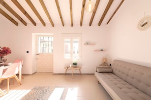 A living room with a sofa, a dining table with chairs, a small table with a plant, and a wall-mounted shelf. - El Patio de Rafaela Country House with Mountain Views, Wi-Fi and Air Conditioning (Alcaucín)