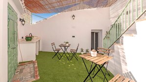 A covered patio with a table and chairs, a small garden area with artificial grass, and a staircase with a green railing. - El Patio de Rafaela Country House with Mountain Views, Wi-Fi and Air Conditioning (Alcaucín)