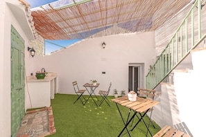 A covered patio with a table and chairs, a small garden area with artificial grass, and a staircase with a green railing. - El Patio de Rafaela Country House with Mountain Views, Wi-Fi and Air Conditioning (Alcaucín)