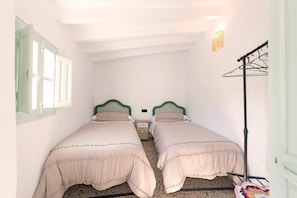 A room with two beds, a window with shutters, a wall-mounted light fixture, and a clothes drying rack. - El Patio de Rafaela Country House with Mountain Views, Wi-Fi and Air Conditioning (Alcaucín)