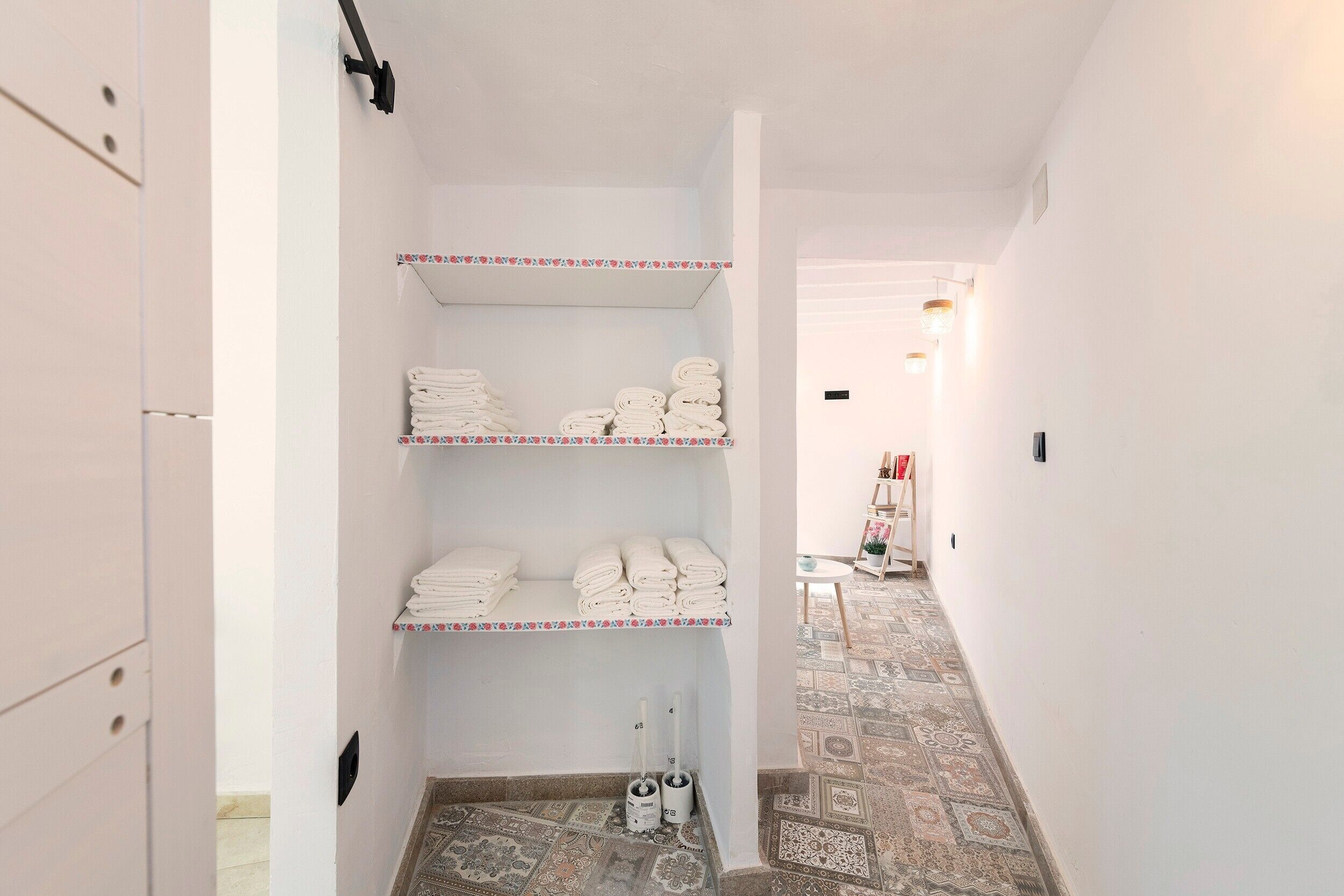 A hallway with white walls, a patterned floor, and shelves with folded towels.
