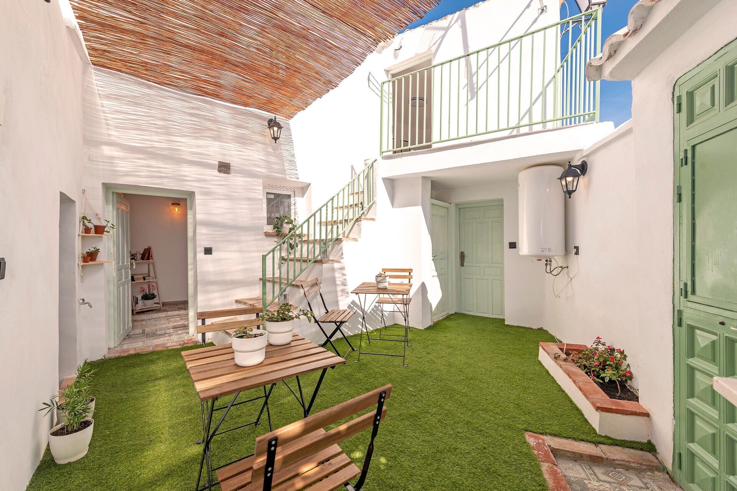 Une cour avec une table et des chaises en bois, une pelouse verdoyante et un bâtiment blanc doté d’un balcon.