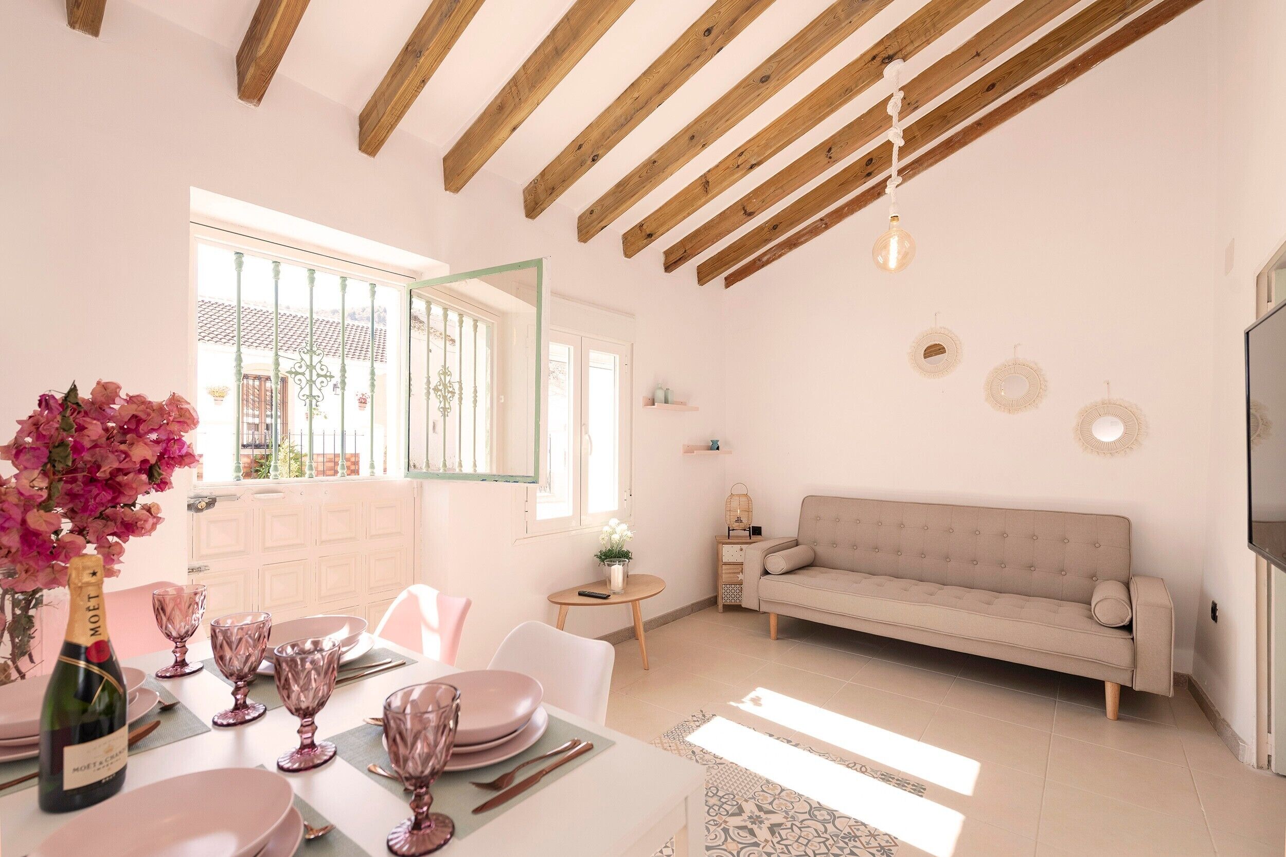 A dining area with a table set for four, a sofa, and a TV mounted on the wall.