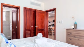 Ein Hotelzimmer mit einem Bett, einer Holzkommode, einem Badezimmer mit Dusche und einem durch eine offene Tür einsehbarer Küchenbereich.