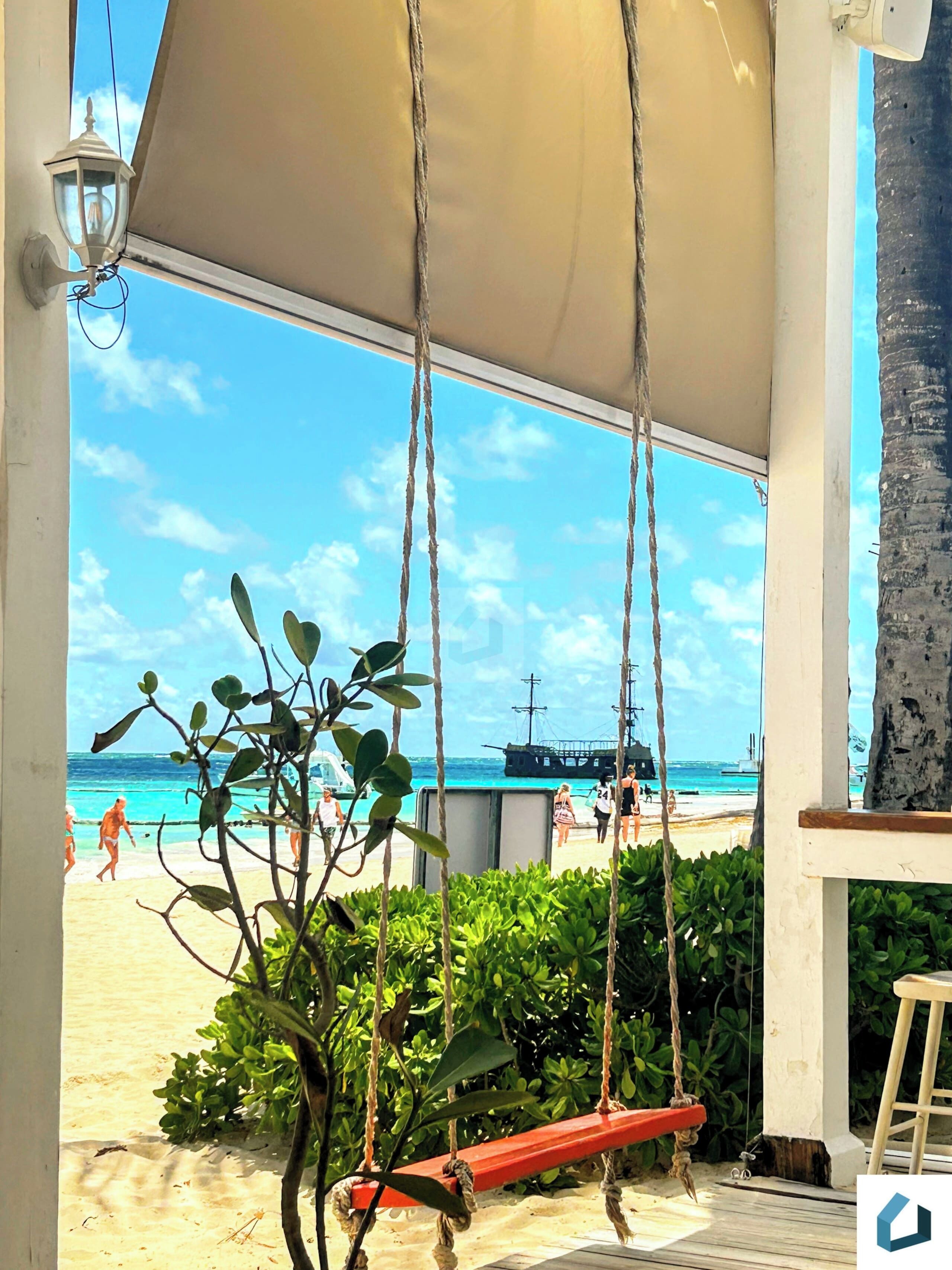 Vista de la playa con un columpio y un barco a lo lejos.