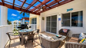 Eine überdachte Terrasse im Freien mit Grill, Korbmöbeln und einem Schild, das die Richtung zum Strand weist.