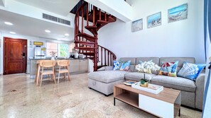 Ein modernes Wohnzimmer mit einem grauen Ecksofa, Holzstühlen, einem Couchtisch und einer Wendeltreppe.