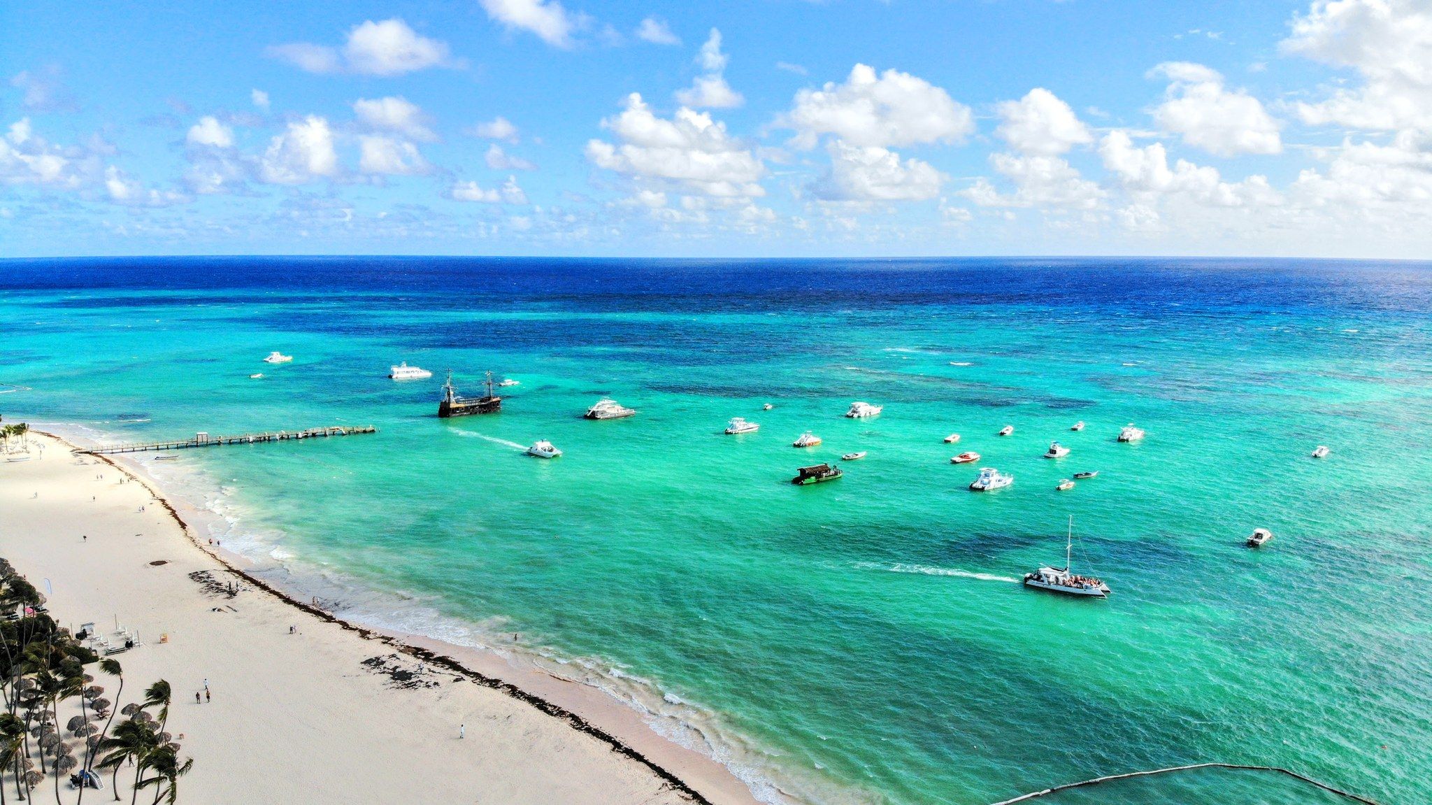 A beach with clear turquoise waters, a pier, and several boats.