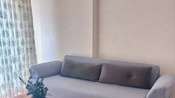 Una sala de estar con un sofá gris, una mesa de centro de vidrio y un jarrón con una planta.