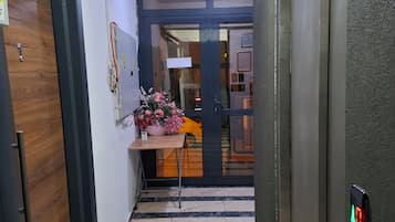 Un pasillo con una puerta de madera, una pequeña mesa con un jarrón de flores y un suelo de baldosas.