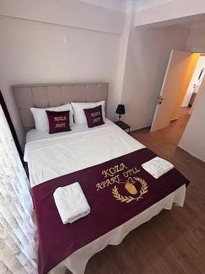 A hotel room with a bed, pillows, a bedside table with a lamp, and a door leading to another room.