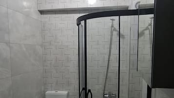 A bathroom with a glass-enclosed shower, a toilet, a sink, and a washing machine.