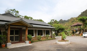 A building with a covered porch, a car parked in front, and a mountainous backdrop. - Reishi Expert B and B (New Taipei City)