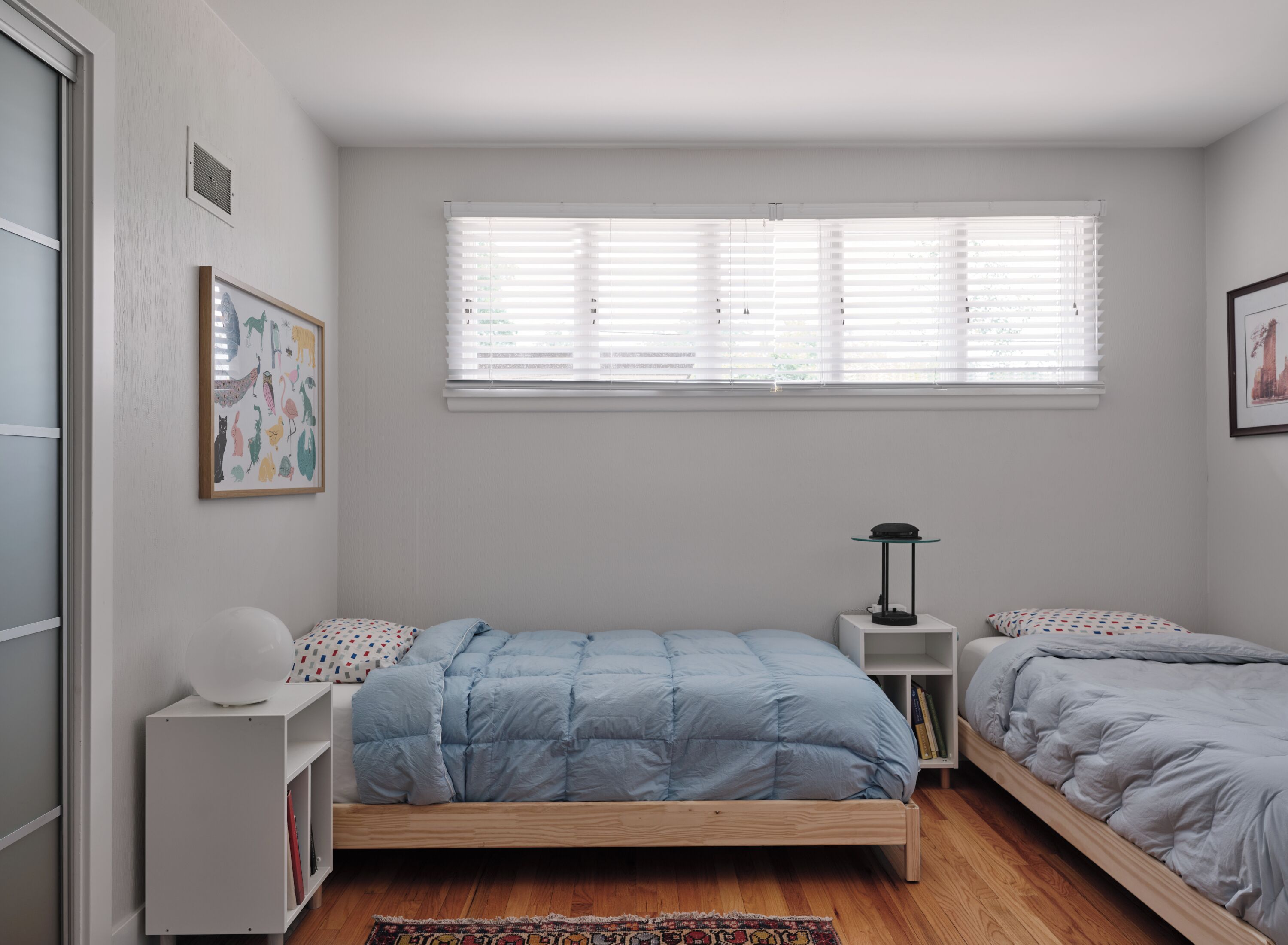 Une chambre à coucher avec un lit simple, une table de chevet, une lampe et une fenêtre avec des stores.
