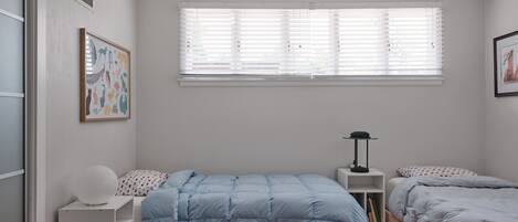 Une chambre à coucher avec un lit simple, une table de chevet, une lampe et une fenêtre avec des stores.