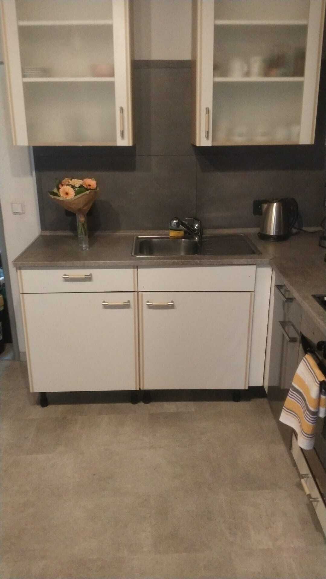 A kitchen with two cabinets, a sink, and a kettle.