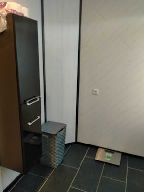 A room with a wardrobe, a small trash bin, and a scale on the floor.