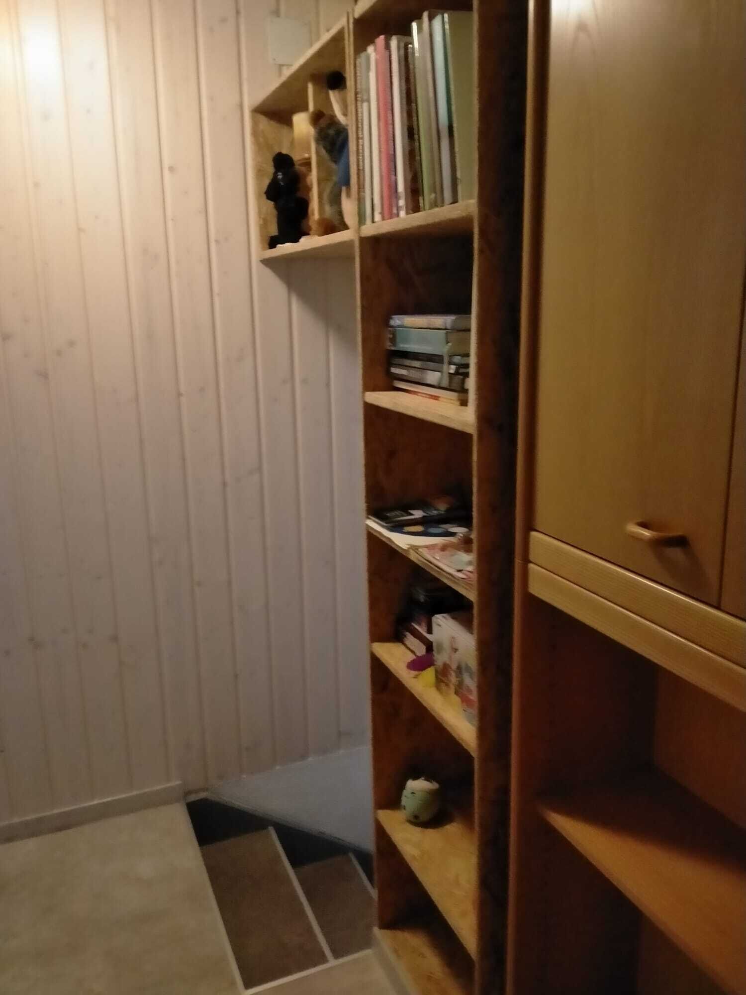 A narrow hallway with wooden paneling on the walls and a wooden bookshelf filled with books and various items.