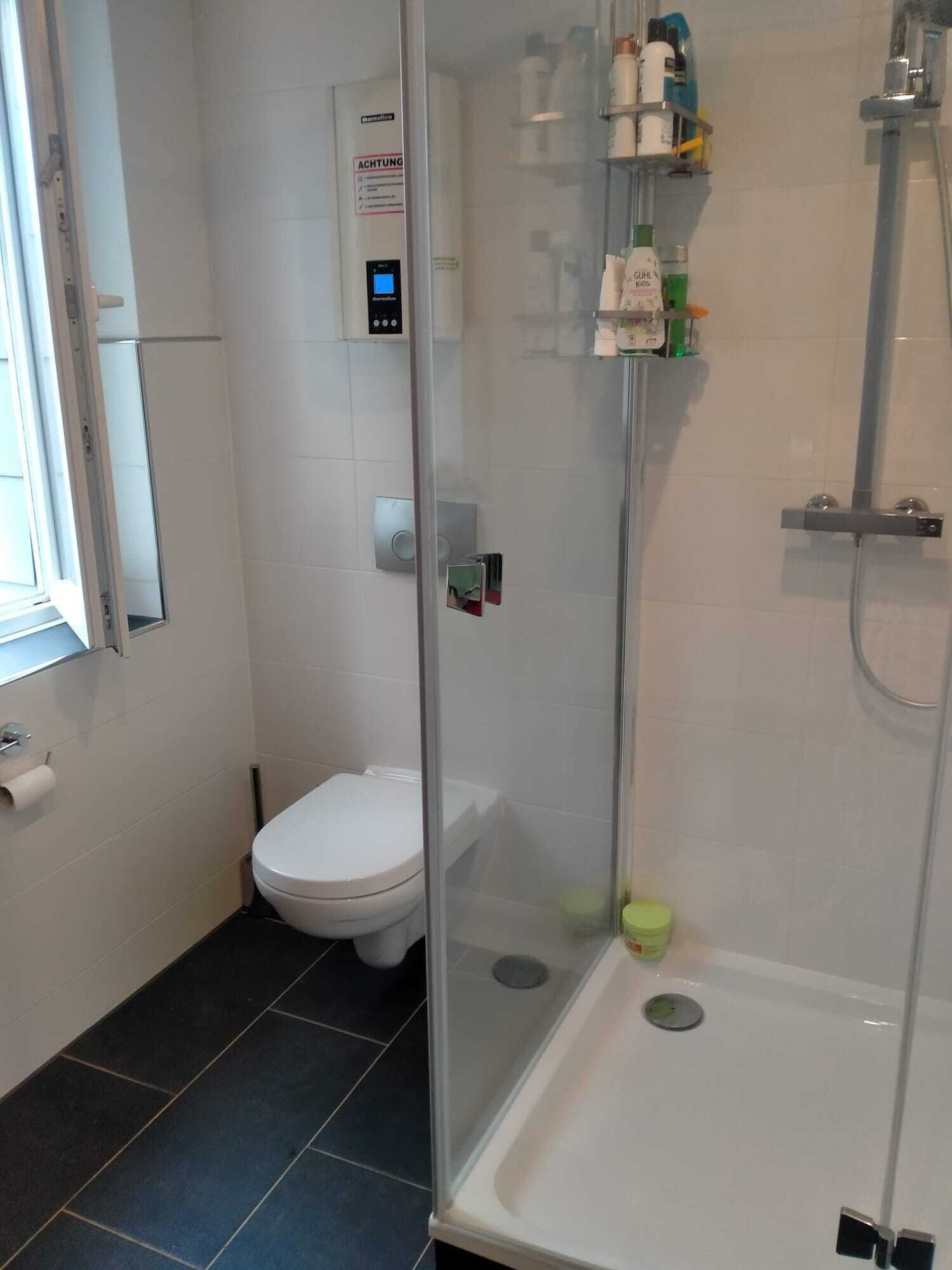 Ein Badezimmer mit Toilette, Duschkabine und Bedienfeld an der Wand.