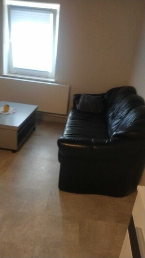 A living room with a black leather sofa, a small table with a yellow object, and a window with blinds. - 🍋 Casa Limone – Your cozy retreat in the Westerwald (not Upland) (Willingen)