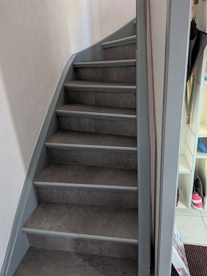 A carpeted staircase with a handrail, leading to a room with a white door and a shelf with items.