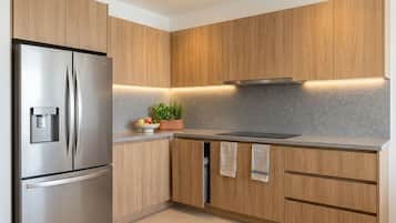 A modern kitchen with wooden cabinets, a stainless steel refrigerator, a built-in oven, and a countertop with a plant and fruits.
