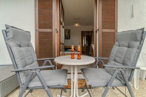A patio with two grey chairs and a small round table, two bottles of Aperol Spritz, and wooden shutters. - Cozy 1-room apartment, sauna, pool, parking (Zwiesel)