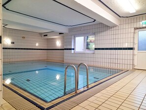 Una piscina interior con paredes de azulejos y zona acuática transparente.