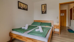 A single bed with a wooden frame, green bedding, and two white towels. There is a bedside table with a lamp and a small drawer. The room has plain walls and a wooden floor. - Cozy 1-room apartment, sauna, swimming pool, parking (Zwiesel)