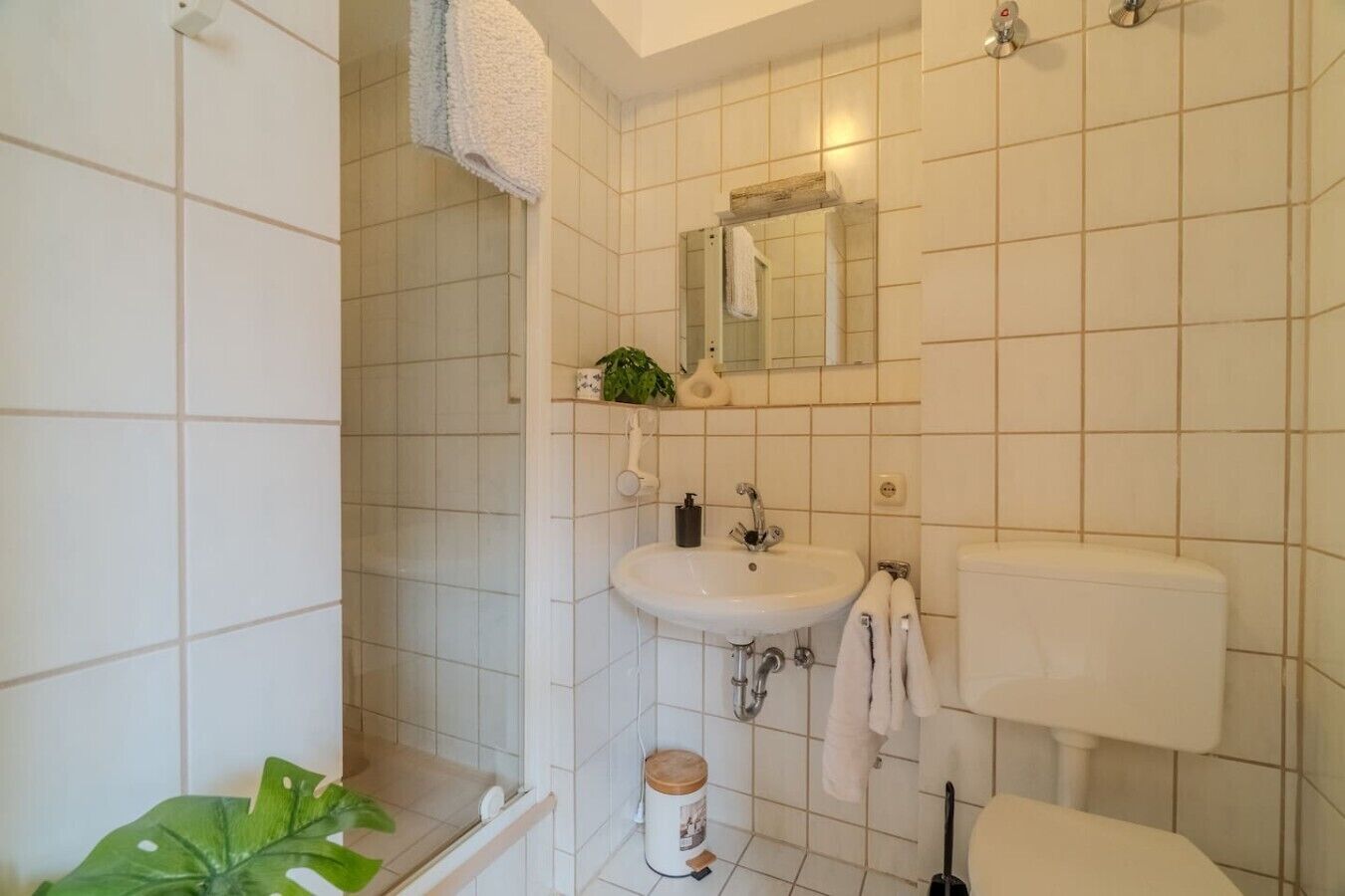 A bathroom with white tiles, a sink, a toilet, and a shower area.
