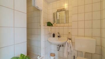 A bathroom with white tiles, a sink, a toilet, and a shower area.