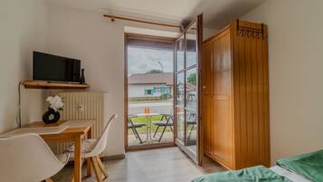 Ein Zimmer mit einem Bett, einem Schreibtisch mit Stuhl, einem Fernseher und Blick ins Freie.