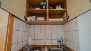 A compact kitchen with a built-in sink, a stove, and a shelf above the sink containing dishes and a carton of milk. - Cozy 1-room apartment, sauna, swimming pool, parking (Zwiesel)