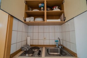 Uma cozinha compacta com pia embutida, fogão e prateleira sobre a pia com pratos e um carton de leite.
