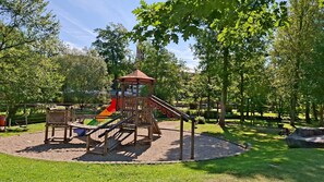 A playground with a slide and climbing structures surrounded by grass and trees. - Cozy 1-room apartment, sauna, pool, parking (Zwiesel)